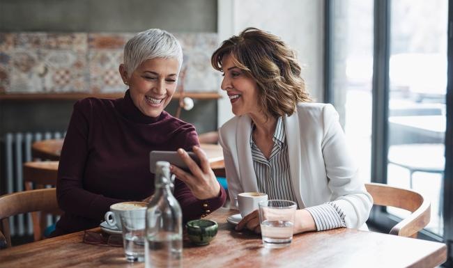 two women sitting at a table looking at a phone